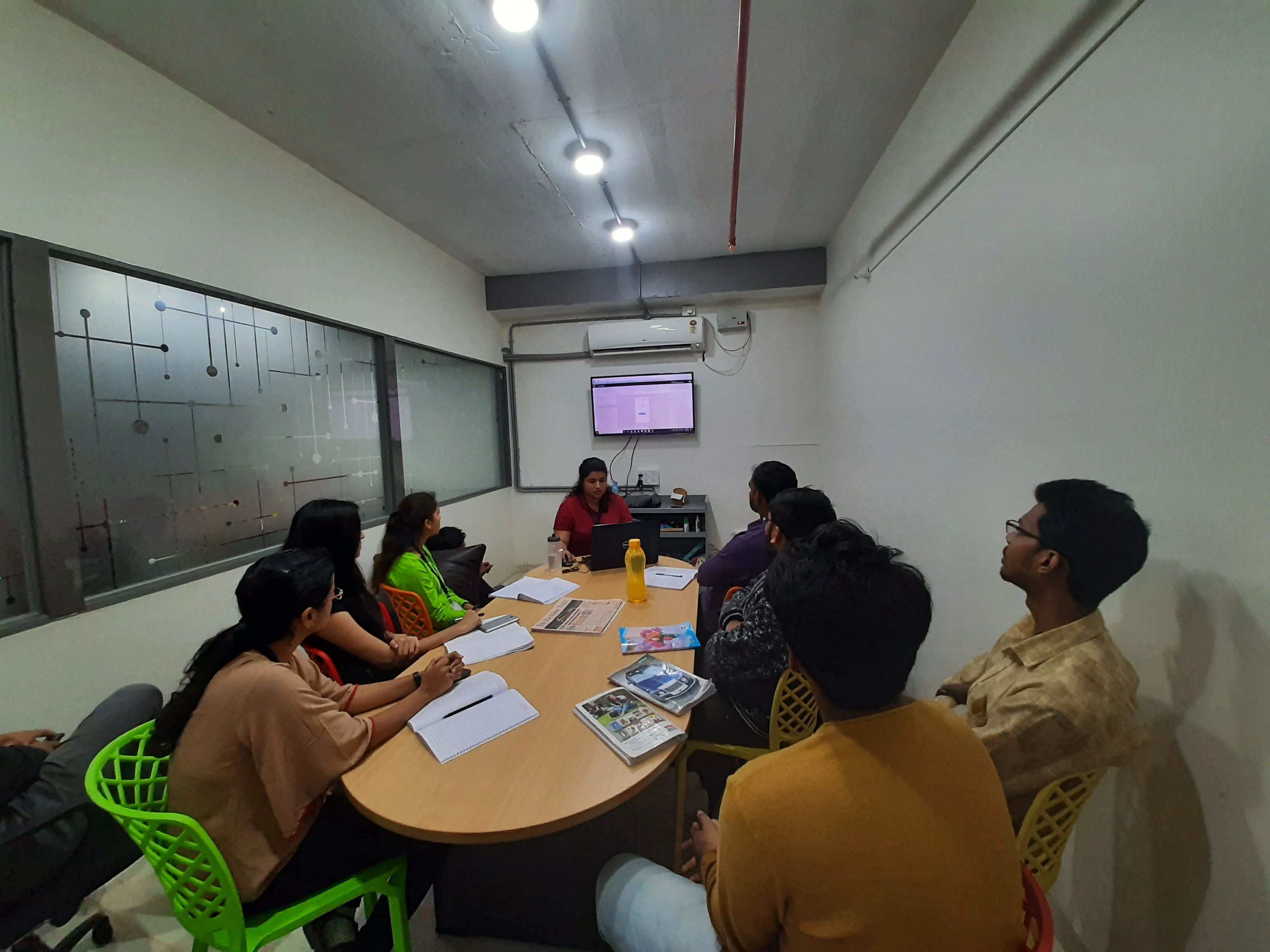 Colleagues in a meeting-room session, notebooks open, a screen at the head of the table