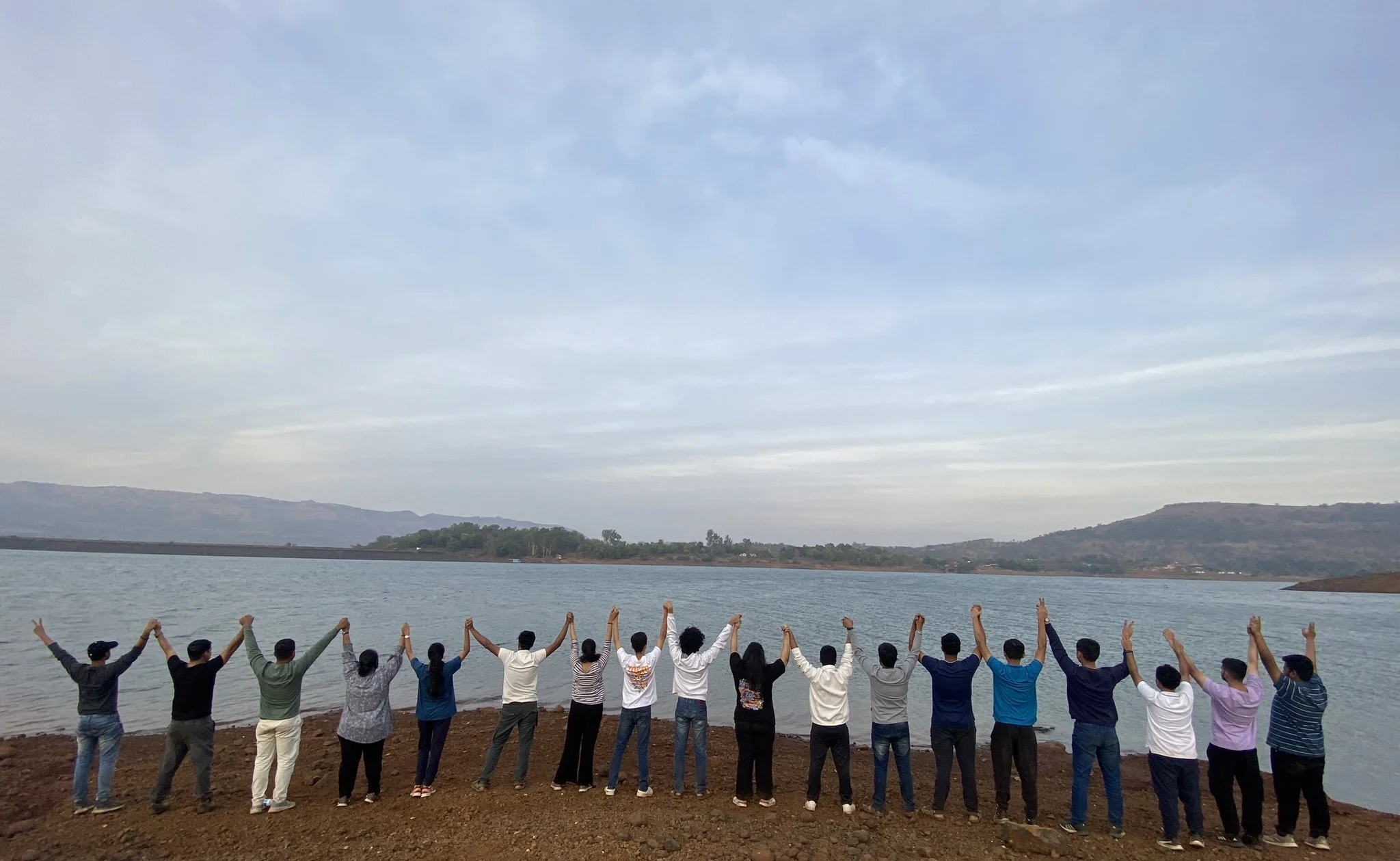 Team members lined up along a lakeshore, hands joined and raised