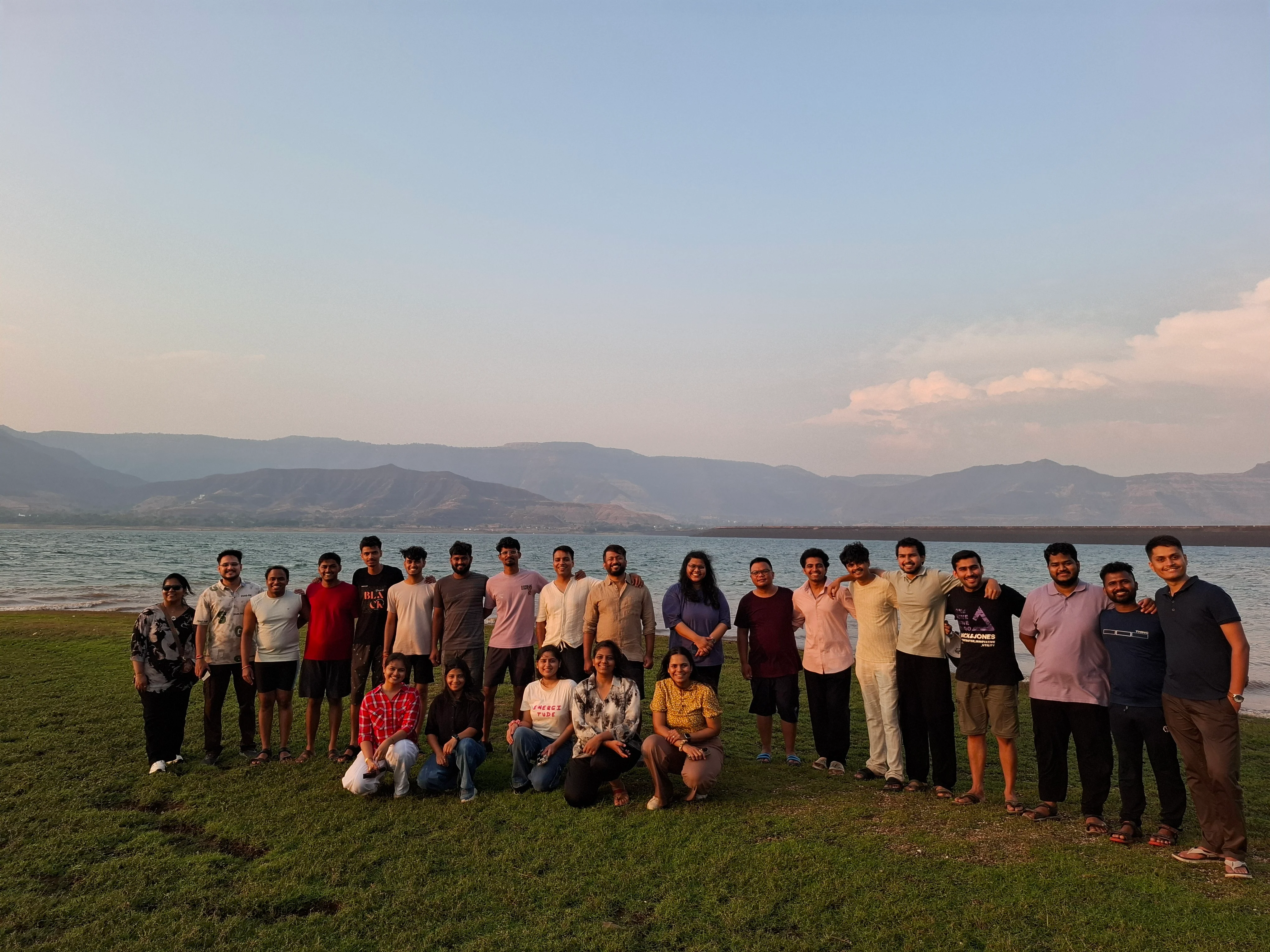The team gathered on a lakeside lawn at dusk, hills behind
